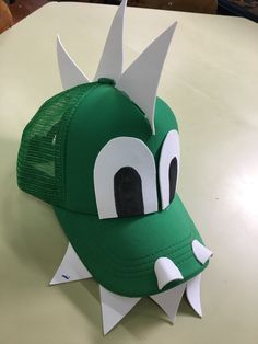 a green hat with white spikes on it's face and mouth is sitting on a table