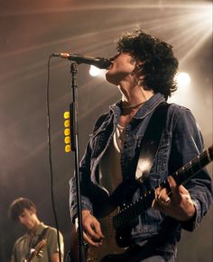 a man singing into a microphone while holding a guitar in front of him on stage