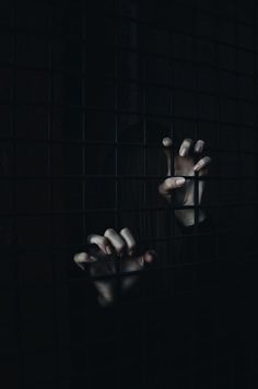 a person holding their hands out through the bars of a caged in area that is dark