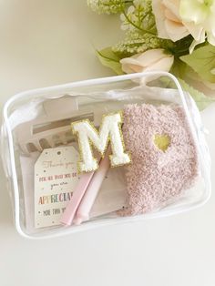 a white plastic container with pink and gold items in it, including a letter m