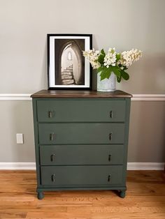 a vase with flowers on top of a dresser next to a framed photo and stairs