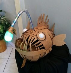 a fish made out of cardboard sitting on top of a black bag next to a potted plant