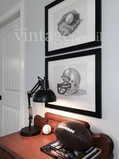 two framed pictures hang on the wall above a desk with a football, lamp and books