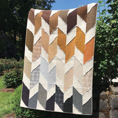 a quilt hanging on a clothes line in front of some trees and bushes with grass