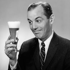 a man in a suit and tie holding up a glass with something on it's side