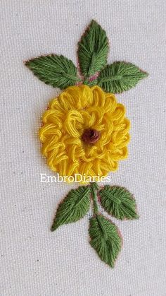 a yellow flower with green leaves is on a white fabric background and has the words embrodiliances written across it