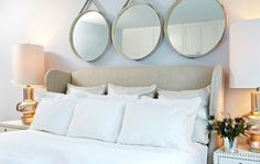 three round mirrors above a bed with white linens and pillows on the headboard