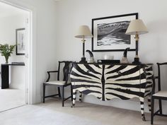 a zebra print dresser and chairs in a room with white walls, black framed art on the wall