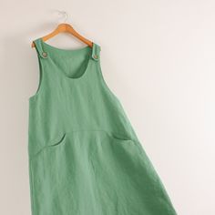 a green dress hanging on a white wall with a wooden hanger in front of it