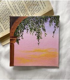 an open book on top of a bed next to a painting with trees in the background