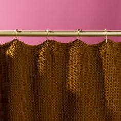 a close up of a curtain on a rod with pink wall in the back ground