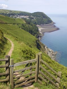 a wooden gate on the side of a grassy hill next to an ocean and beach