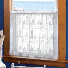 a window in a blue room with a white curtain and sailboats on the water