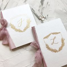 two wedding cards with gold monogrammed initials and pink ribbon tied around the edges