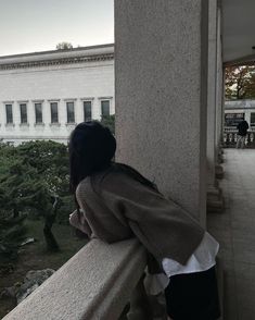 a person sitting on a ledge looking out at the trees and building in the distance