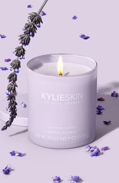 a white candle sitting on top of a table next to purple and lavender flowers in front of it