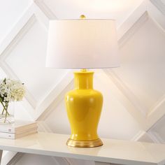 a yellow vase sitting on top of a white table next to a lamp and books