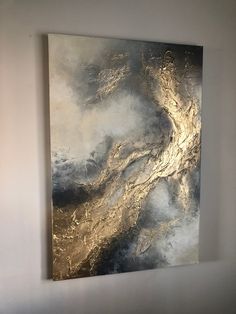 an abstract painting hanging on the wall in a white room with a black and gold design