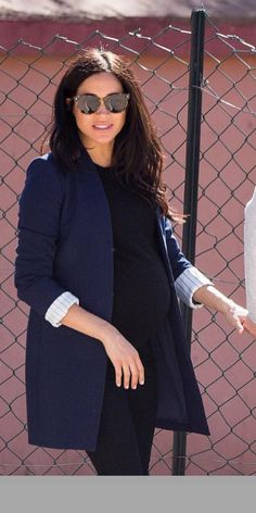 the pregnant woman is walking down the street in her black dress and coat, with sunglasses on