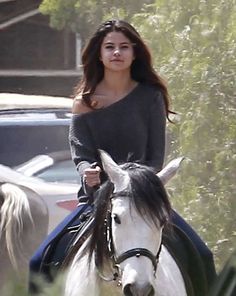 a woman riding on the back of a white horse in front of a parked car