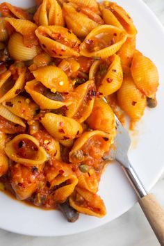 a white plate topped with pasta covered in sauce next to a wooden spatula on top of a marble counter