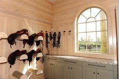 there are many horse saddles hanging on the wall in this room with two windows