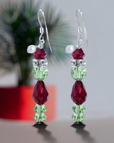 pair of earrings with red, green and white beads on table next to potted plant