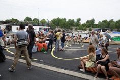 a group of people sitting on top of a parking lot next to a river with boats in the background