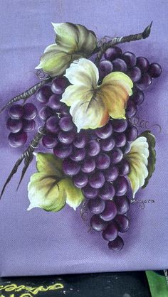 a painting of some grapes on a purple board with leaves and flowers painted on it