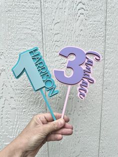 a hand holding a blue and purple number three cake topper with the number three on it