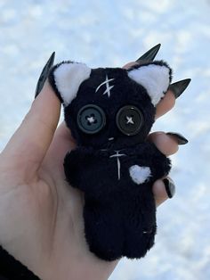 a hand holding a small black and white stuffed animal with big eyes on it's face