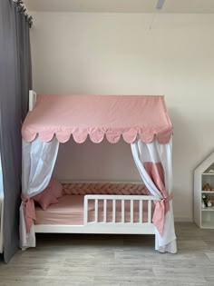 a pink and white canopy bed with curtains on the top, next to a window