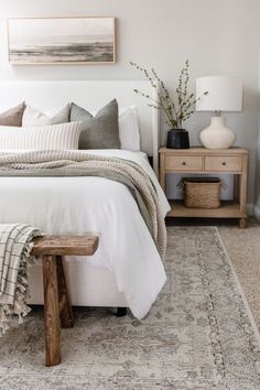 a white bed with pillows and blankets on top of it next to a wooden bench