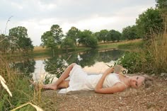 a woman laying on the ground next to a body of water with trees in the background