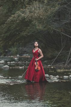 a woman in a red dress is standing in the water holding a violin and looking up into the sky