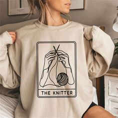 Cozy up in our 'The Knitter' Sweatshirt, the perfect blend of comfort and creativity for those who adore the art of knitting. Inspired by the timeless Tarot cards, this sweatshirt is a trendy tribute to your knitter's pride. Ideal for both crafting at home or showcasing your hobby out and about, it's a staple piece for any knitting enthusiast. The soft fabric ensures warmth and ease, while the unique design speaks to your artistic side. A wonderful gift for knitters, this sweatshirt is a snug an Funny Knitting, Knitting Shirt, Knitting Humor, The Knitter, Knitting Gift, Knit Shirt, Staple Pieces, Tarot Card, Sew-in Labels