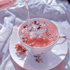 water being poured into a teacup filled with ice and pink flowers on a white table cloth