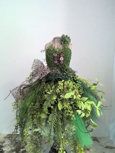 a mannequin made out of green plants and other greenery sits on a table