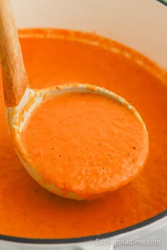 a wooden spoon full of tomato soup in a pot