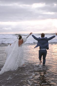 a bride and groom running into the ocean