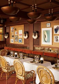 a dining room with tables and chairs covered in white tablecloths, framed pictures on the wall