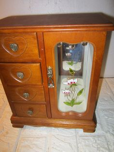 a wooden cabinet with glass doors and flowers on the front door, sitting on a white tile floor