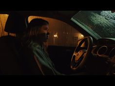 a woman sitting in the driver's seat of a car with rain on the windshield