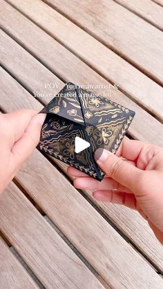 two hands are holding an origami piece on a wooden bench with text overlay