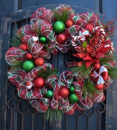 a wreath with christmas decorations hanging on the front door, next to an iron gate