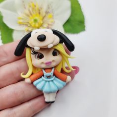 a hand holding a tiny doll with a flower in the background