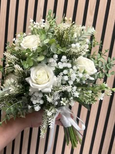 a bouquet of white roses and greenery in someone's hand on a striped background