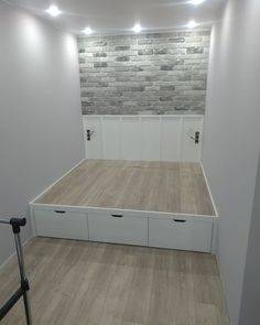 an empty room with white storage drawers and brick wall behind the bed, in front of a wooden floor