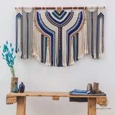 a wooden table topped with a blue vase filled with flowers next to a wall hanging