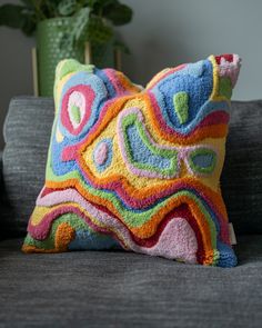 a colorful pillow sitting on top of a couch next to a green potted plant